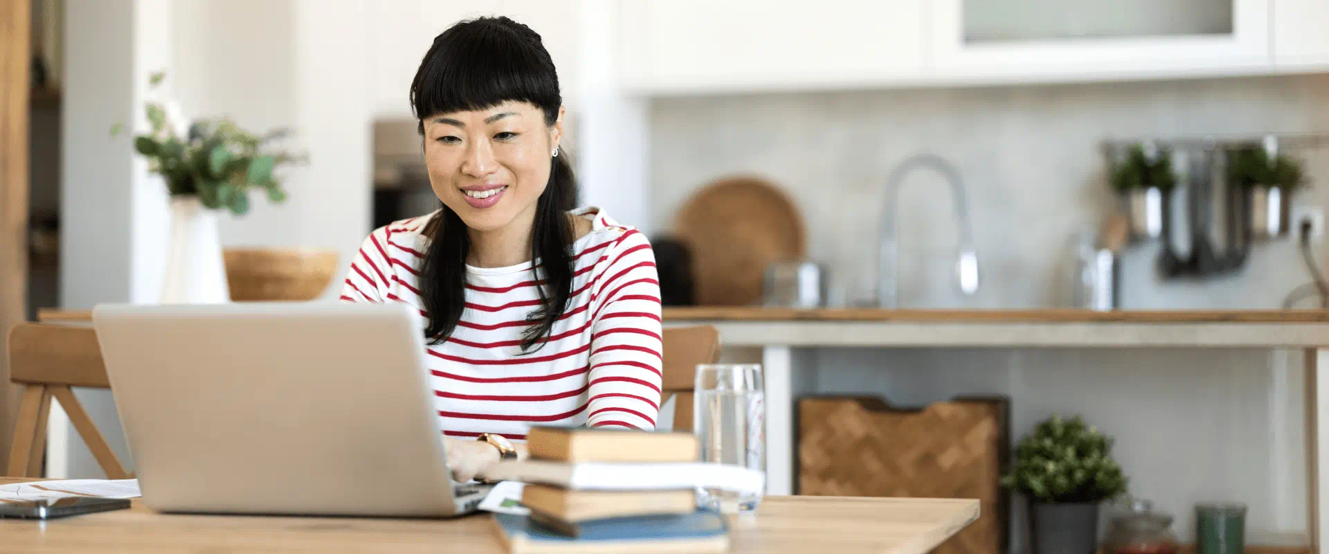 A person sits, writing at their laptop in their kitchen