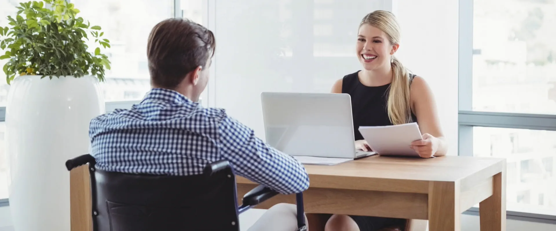 An interviewer sits across the desk from a man in a wheelchair.