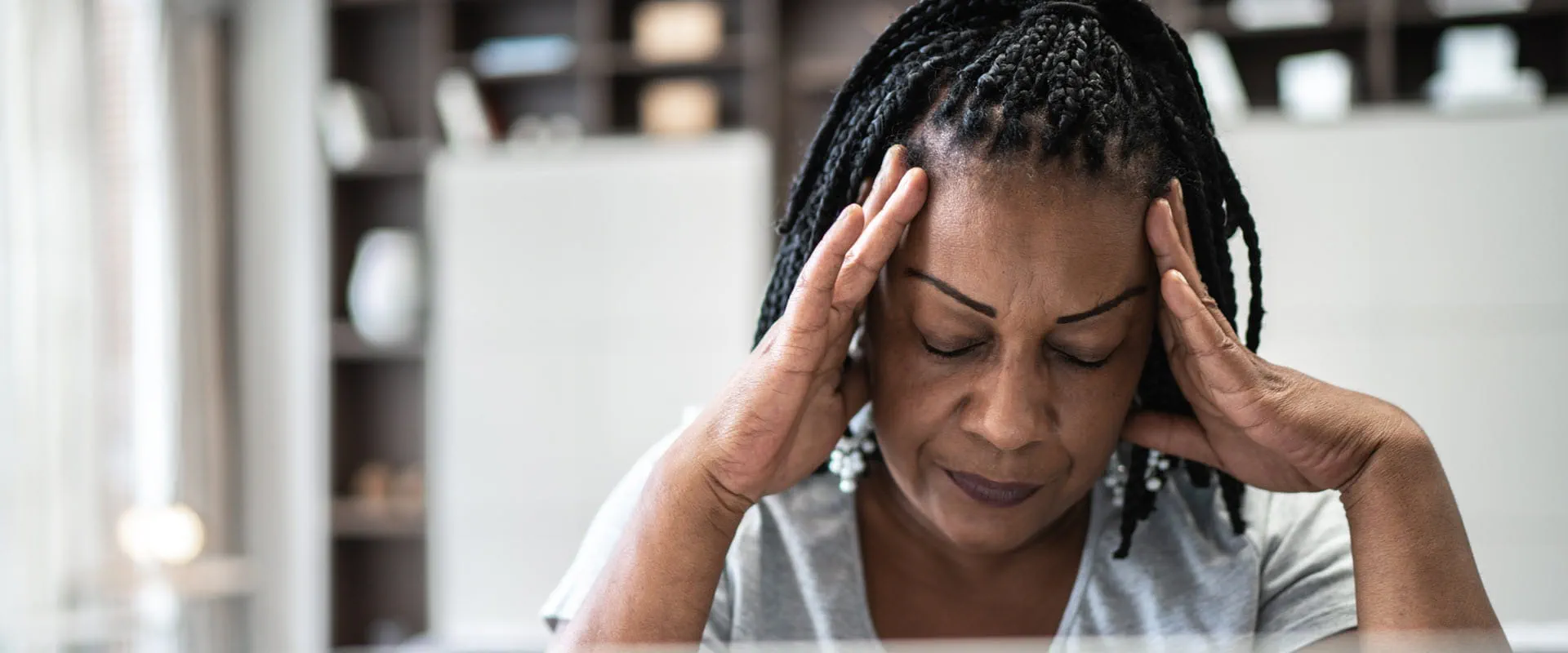 A middle-aged woman sits at home in front of her laptop. Her head is in her hands, seeming stressed.