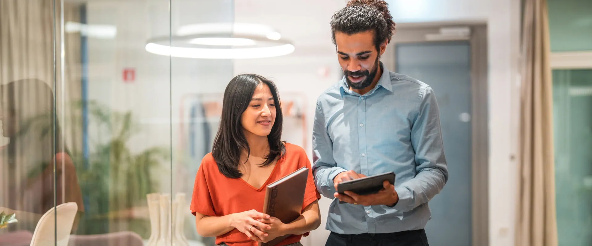 Two coworkers walking in office looking at a digital tablet.