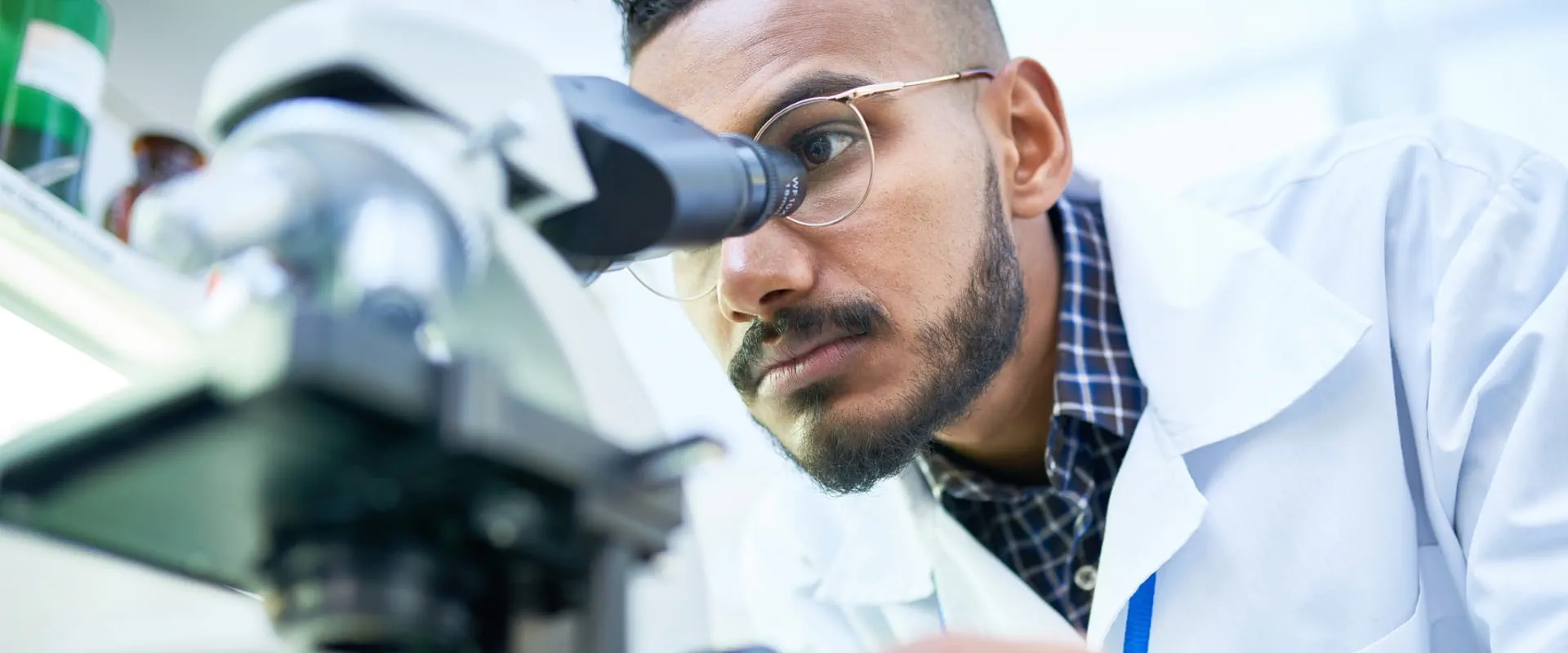 A person in a lab coat looks into a microscope