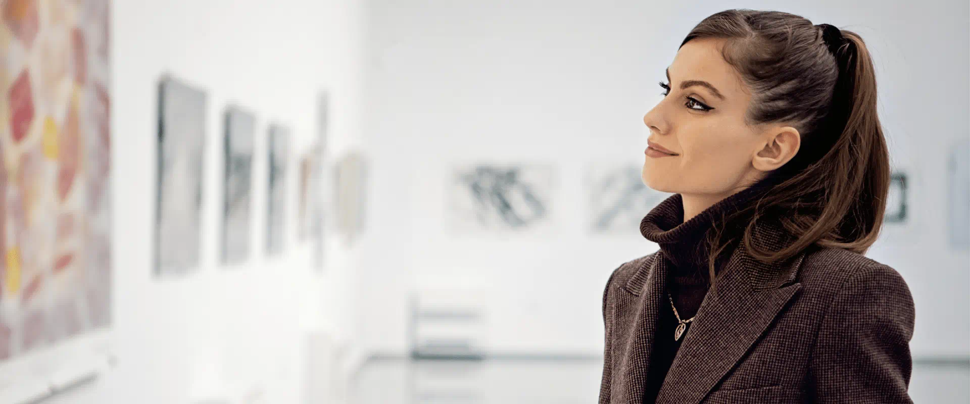 A well-dressed person standing in an art museum gallery with paintings on the walls.