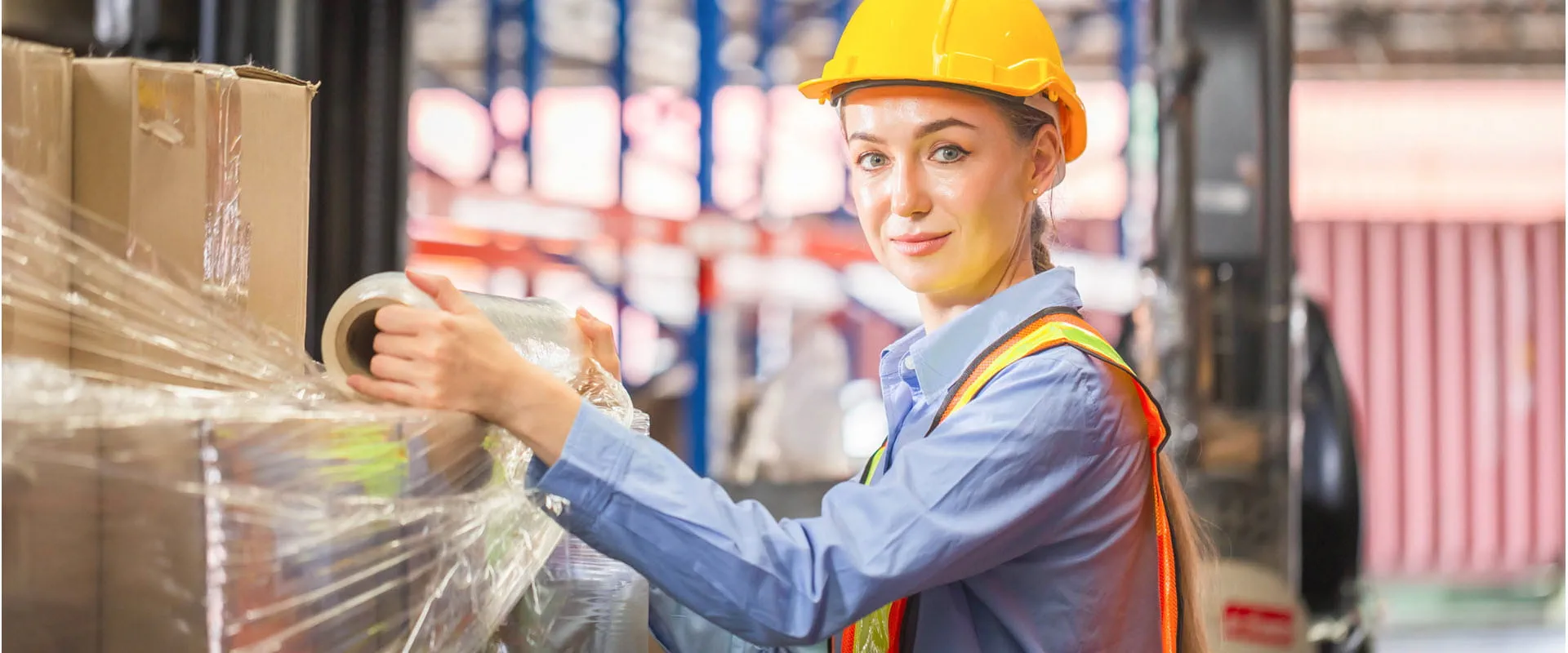 Worker wrapping boxes in stretch film at warehouse.