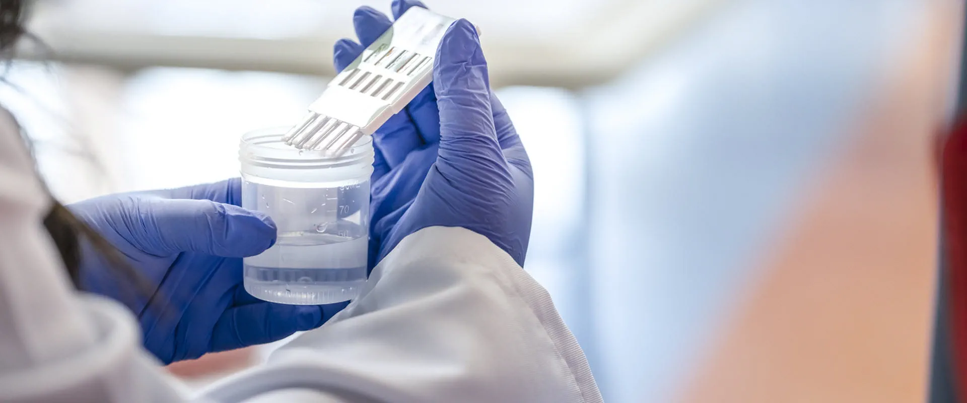 blue gloved hands performing medical test in glass beaker