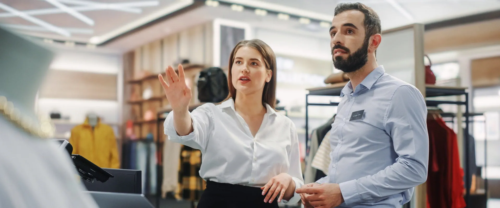 Two retail workers, dressed professionally, look at something out of sight in a high-end retail store.