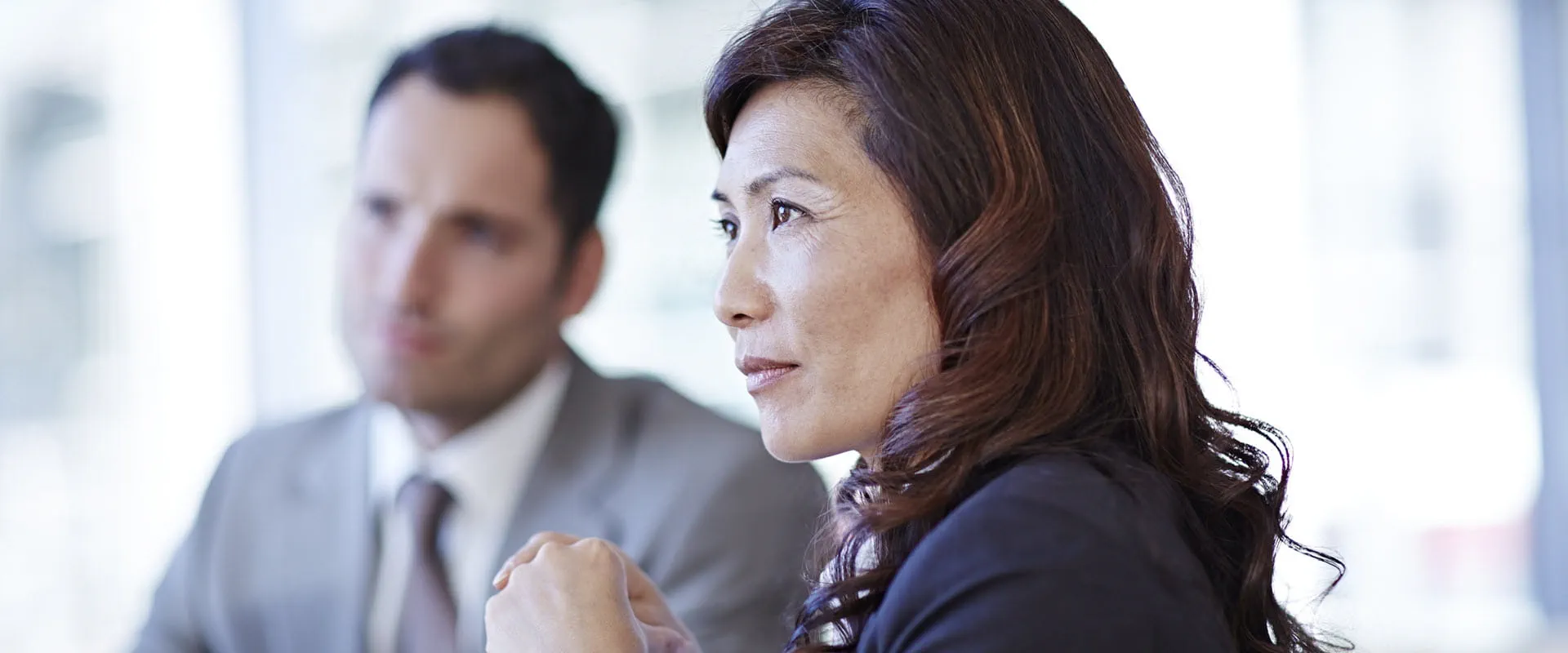 A business woman sits at a conference room table, a male coworker sits next to her out-of-focus