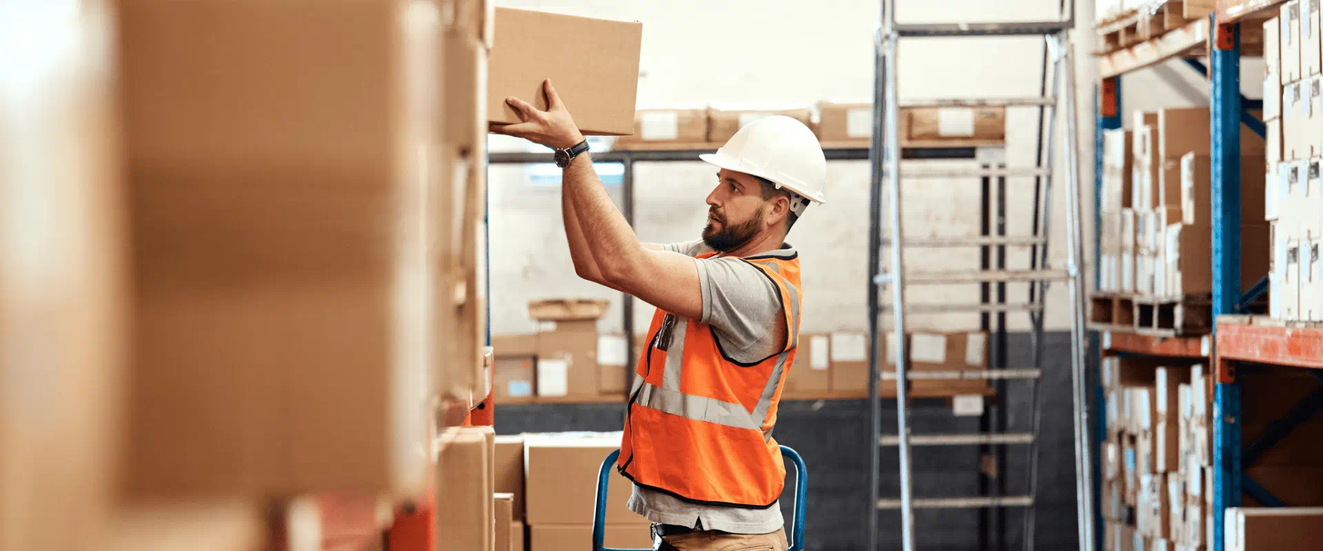 A worker in a warehouse places a box on a high shelf