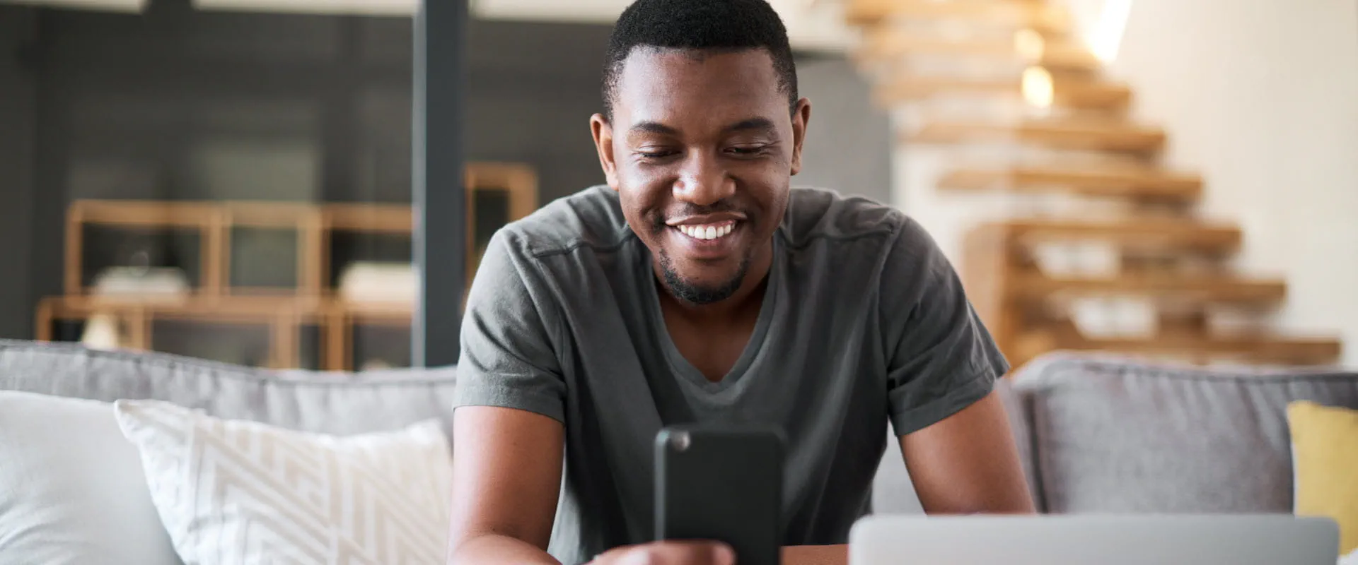A person sits in their living room, smiling and looking at their phone