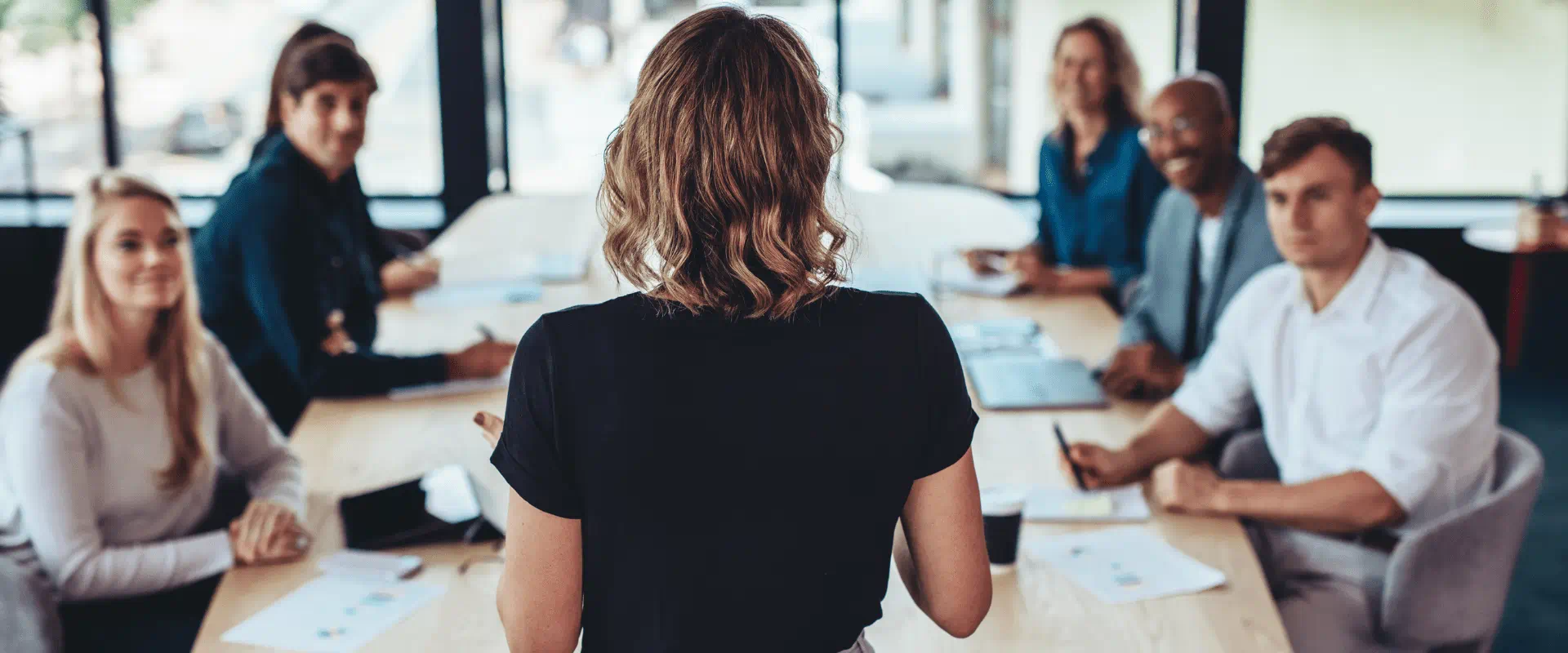 A group of people sit at a conference table looking up at someone who is speaking. 