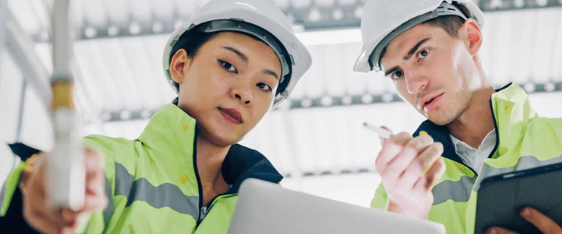 Two people in hardhats and safety vests inspect a machine