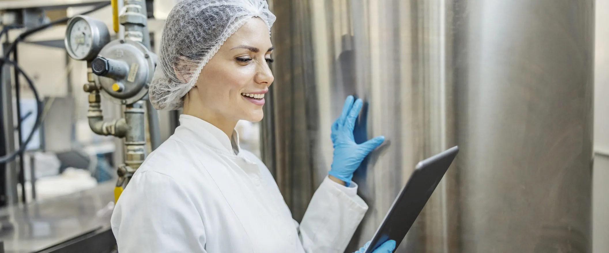A worker in food safety coverings, looks at a clipboard in in food processing facility