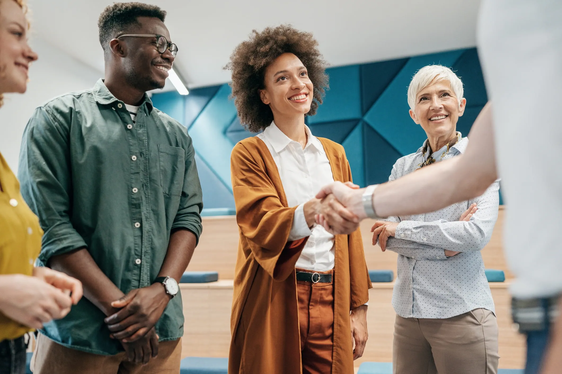 A group of workers of various ages stand in a circle. One of them is shaking the hand of someone out of frame