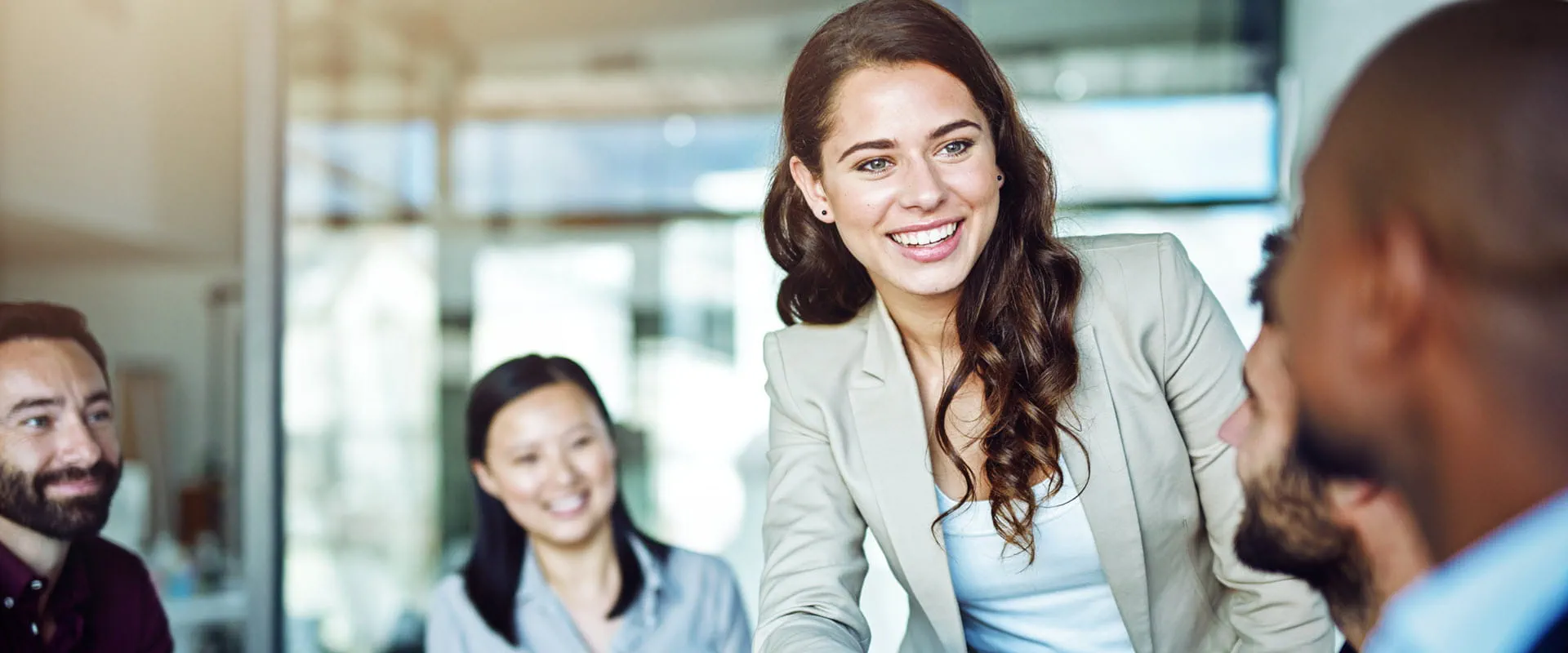 A smiling person in business attire reaches across a table to shake hands during a professional meeting. 