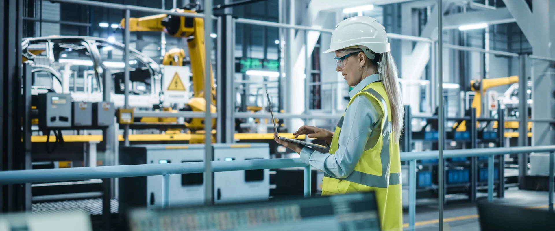 Automotive engineer wearing hard hat, standing, using a laptop.