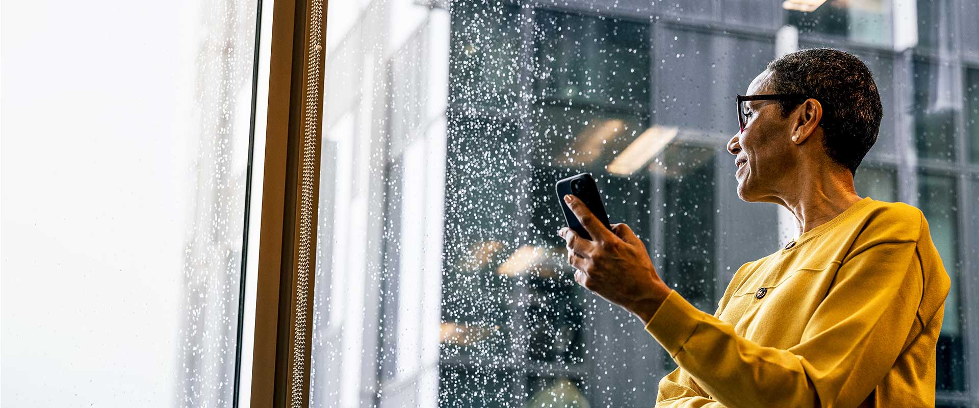  Woman holding phone, gazing at rainy city view