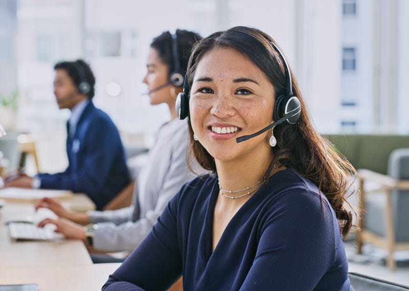 A office worker wearing a headset is smiling and sitting at a desk in an office environment