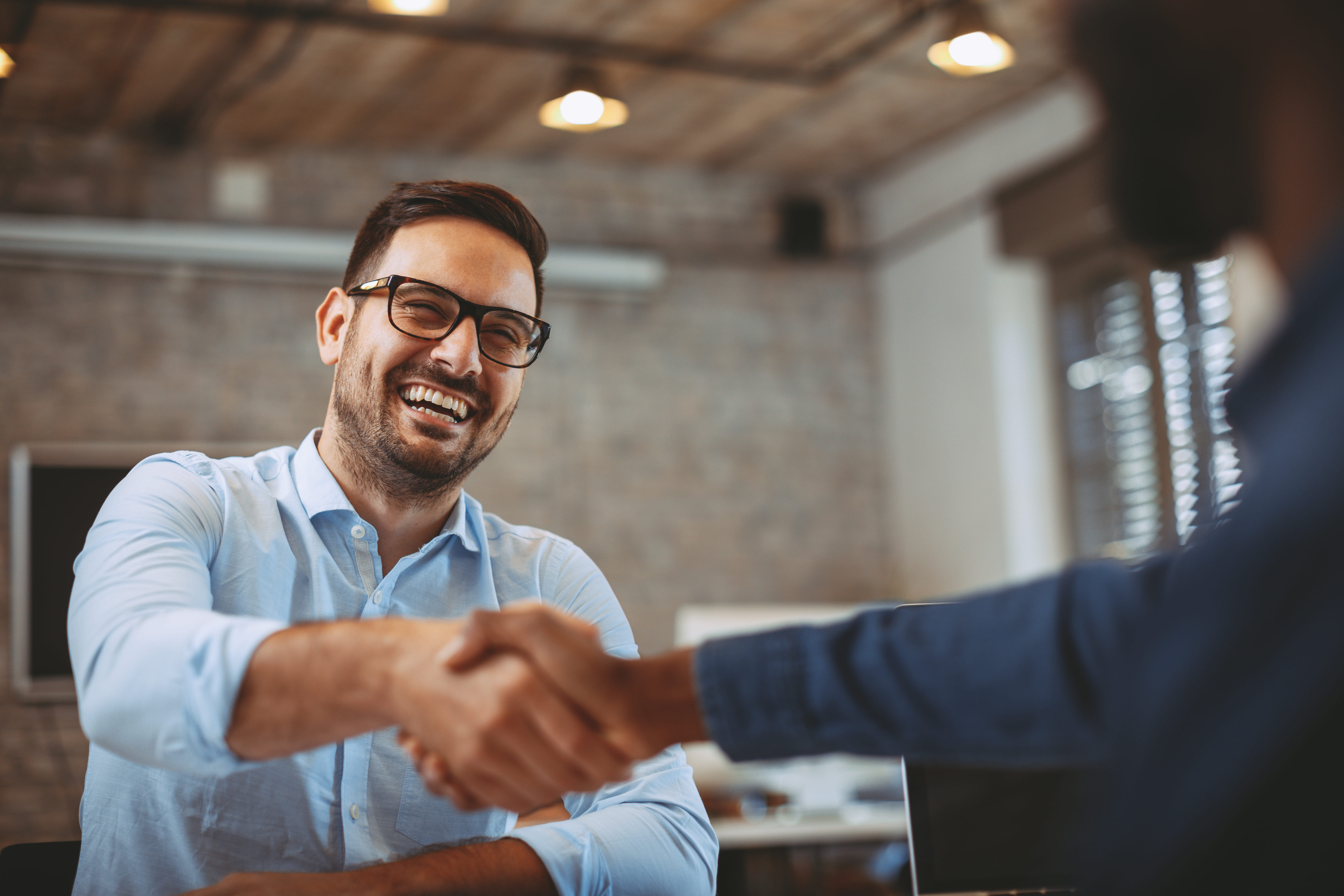 Two smiling professionals shaking hands in a modern office, symbolizing successful collaboration and partnership.