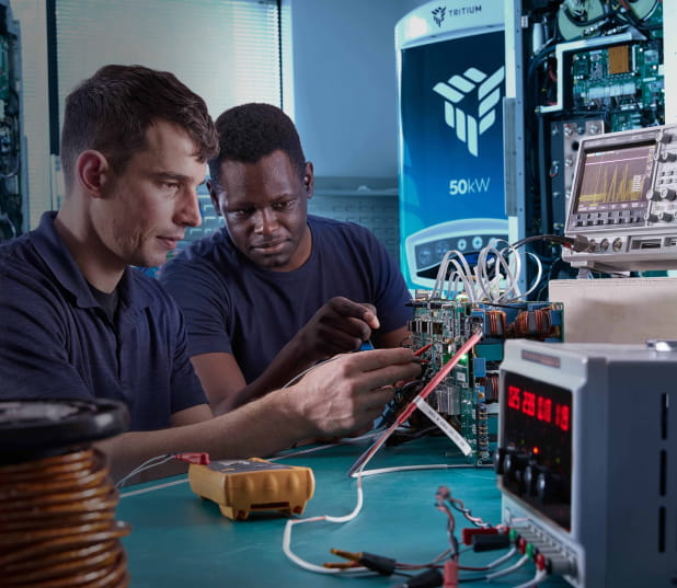 Two technicians working on electronic equipment in a high-tech workspace, surrounded by tools and devices.