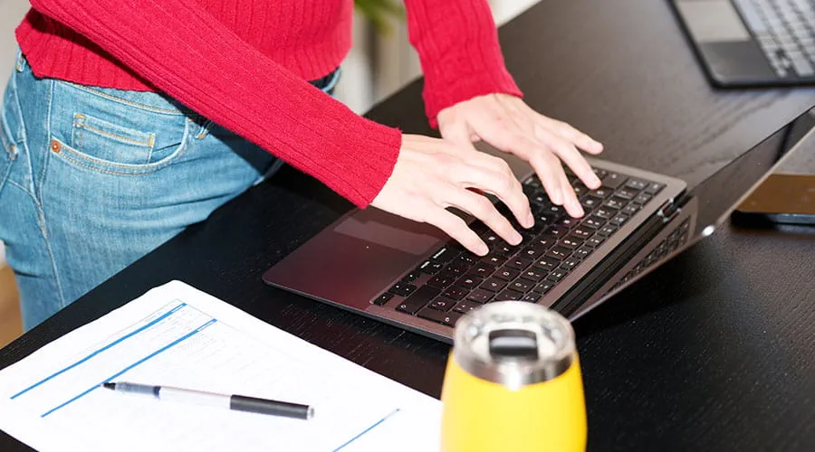 Persona che lavora al computer portatile alla scrivania con una tazza di caffè.