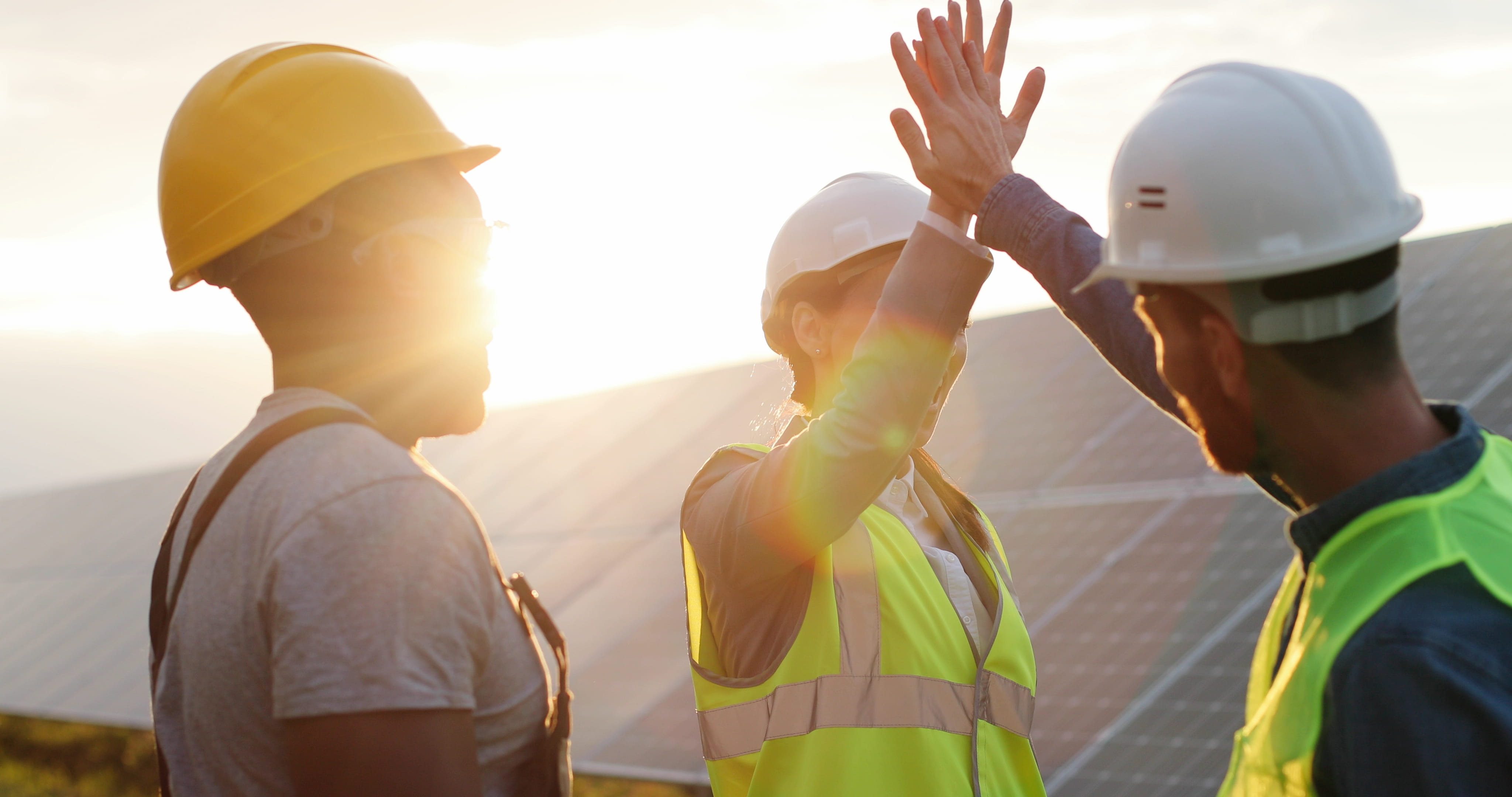 Fornøyde bygningsarbeidere gir hverandre  high-five ved solcelleanlegg i solnedgang.